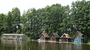 Fileira de cabanas de madeira à beira de um lago, rodeadas por árvores densas.