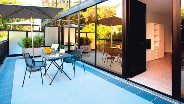 An outdoor patio with a table and chairs, a large umbrella, and a glass wall leading to an interior space. - Residence Riviera Palace, Loano (Loano)