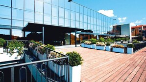 A modern building with large glass windows, a wooden deck, and outdoor seating areas with planters. - Residence Riviera Palace, Loano (Loano)