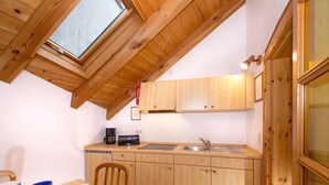 Eine kleine Küche mit Holzschränken, einem Esstisch und einem Fenster über der Spüle.