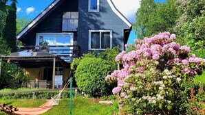 A two-story house with a dark blue exterior, a covered patio area, and a hammock. - Holiday Home Right on the Lake, Florczaki (Lukta)