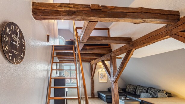 A loft-style room with exposed wooden beams, a loft bed, a staircase, and a clock on the wall. - Studio in Buchholz am Muritzsee (Buchholz)