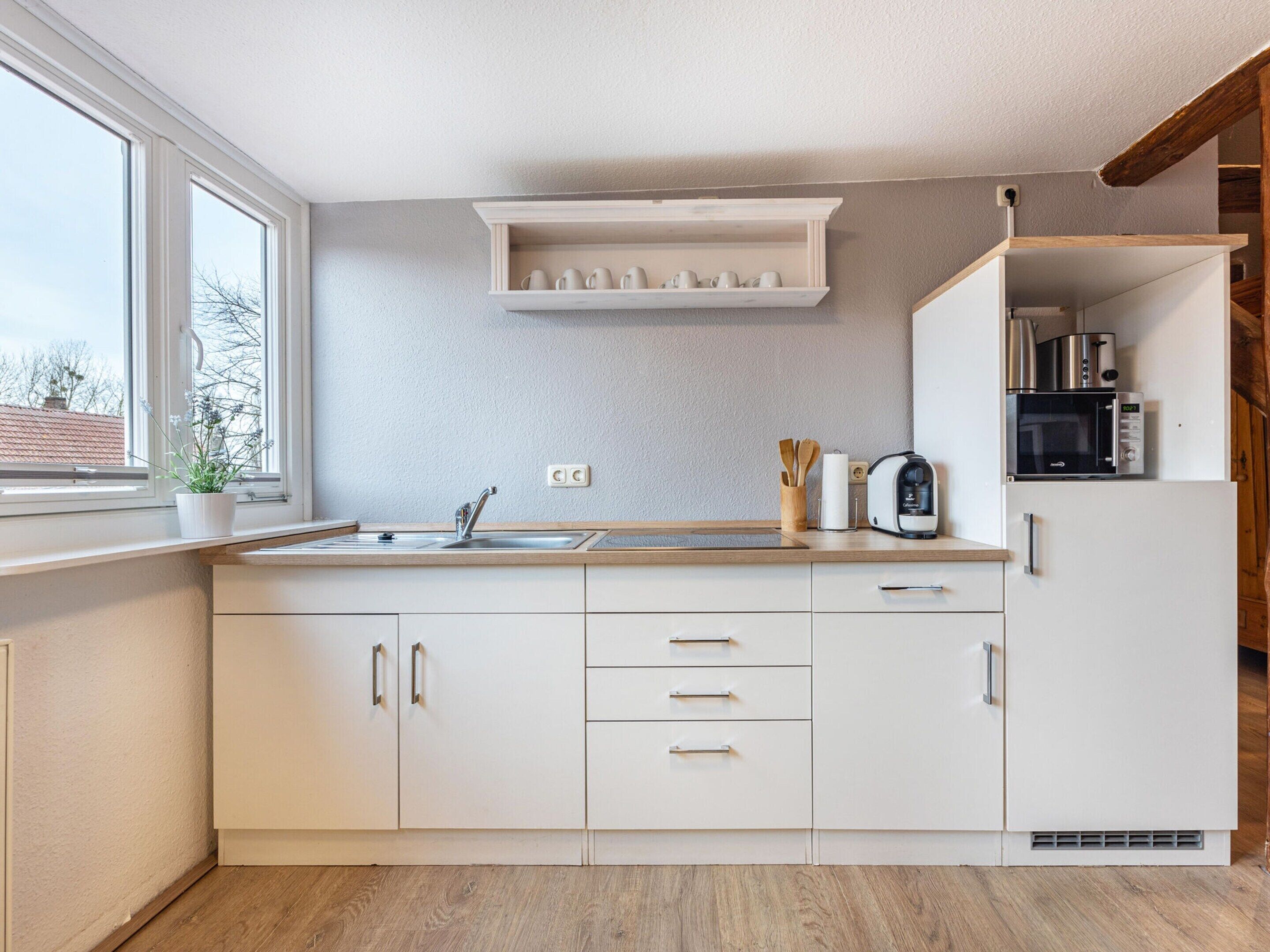 A modern kitchen with white cabinets, a wooden countertop, a built-in shelf above the sink, and a window providing natural light.