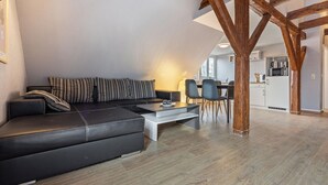 A modern loft-style living area with a black leather sofa, striped pillows, and a dining table with chairs. A kitchen with white appliances is visible in the background. - Studio in Buchholz am Muritzsee (Buchholz)