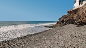 Une plage rocheuse avec un bâtiment situé sur une falaise surplombant la mer.