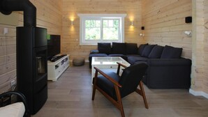 Interior acolhedor de uma cabana de madeira com lareira, um sofá, uma mesa de centro e uma televisão.