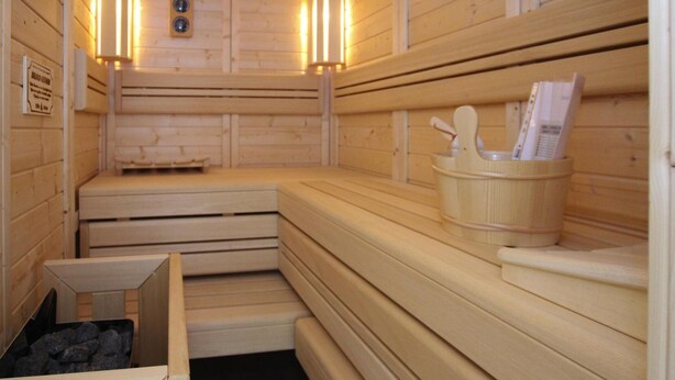 Uma sauna com bancos de madeira, um banco de madeira com suporte para toalha e uma pequena caixa de madeira com pedras.