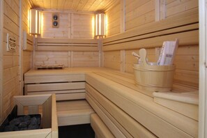 Un sauna avec des bancs en bois, un banc en bois muni d’un porte-serviettes et une petite boîte en bois contenant des pierres.