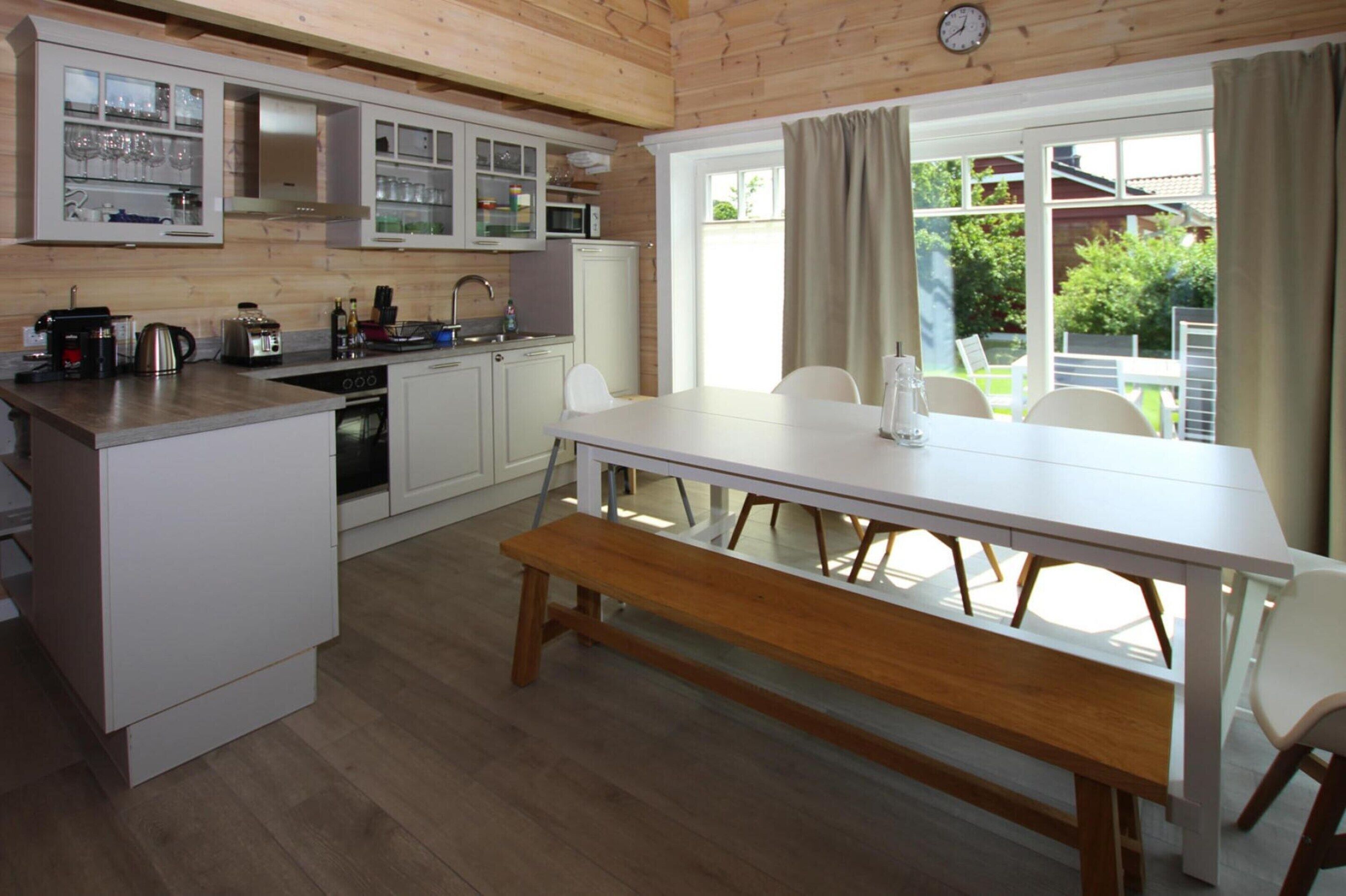 Una cocina moderna con armarios blancos, encimera de madera y un comedor con mesa y banco blancos.