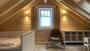 Quarto de sótão aconchegante com paredes de madeira, teto inclinado, janela, cama, cadeira e uma pequena mesa.