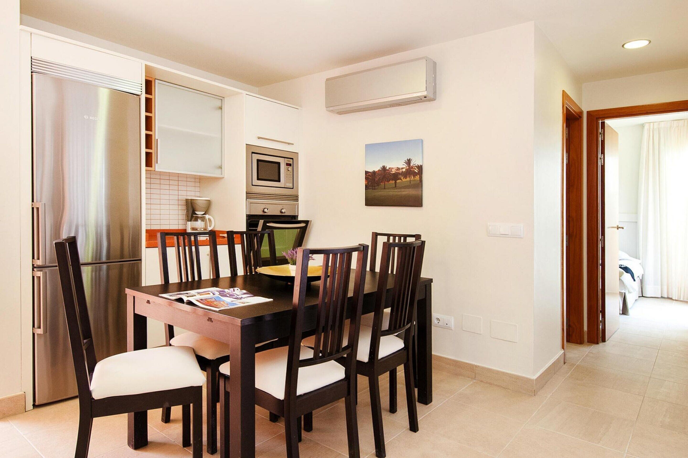 Une cuisine moderne équipée d’une table à manger, de chaises, d’un réfrigérateur, d’un four, d’un four à micro-ondes et d’un appareil de climatisation.