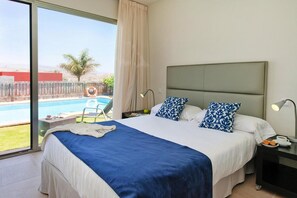 A hotel room with a large bed, two bedside lamps, a nightstand, and a view of a swimming pool. - Holiday Home in Maspalomas With Private Pool (San Bartolomé de Tirajana)