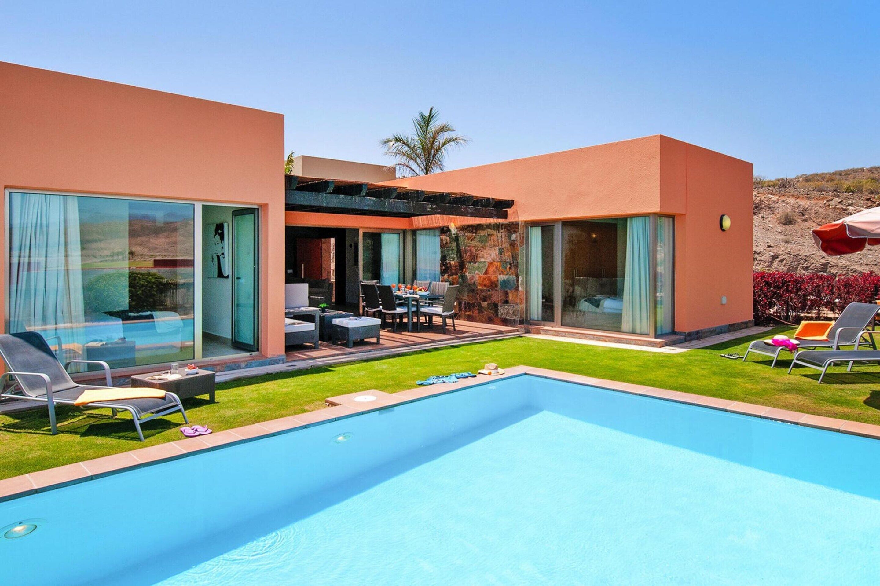 A modern poolside area with a clear blue pool, sun loungers, and a patio with outdoor furniture.