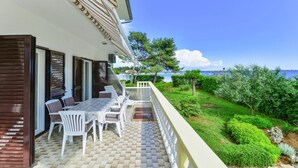 Un balcon avec une table et des chaises, donnant sur un jardin aménagé et un plan d’eau.