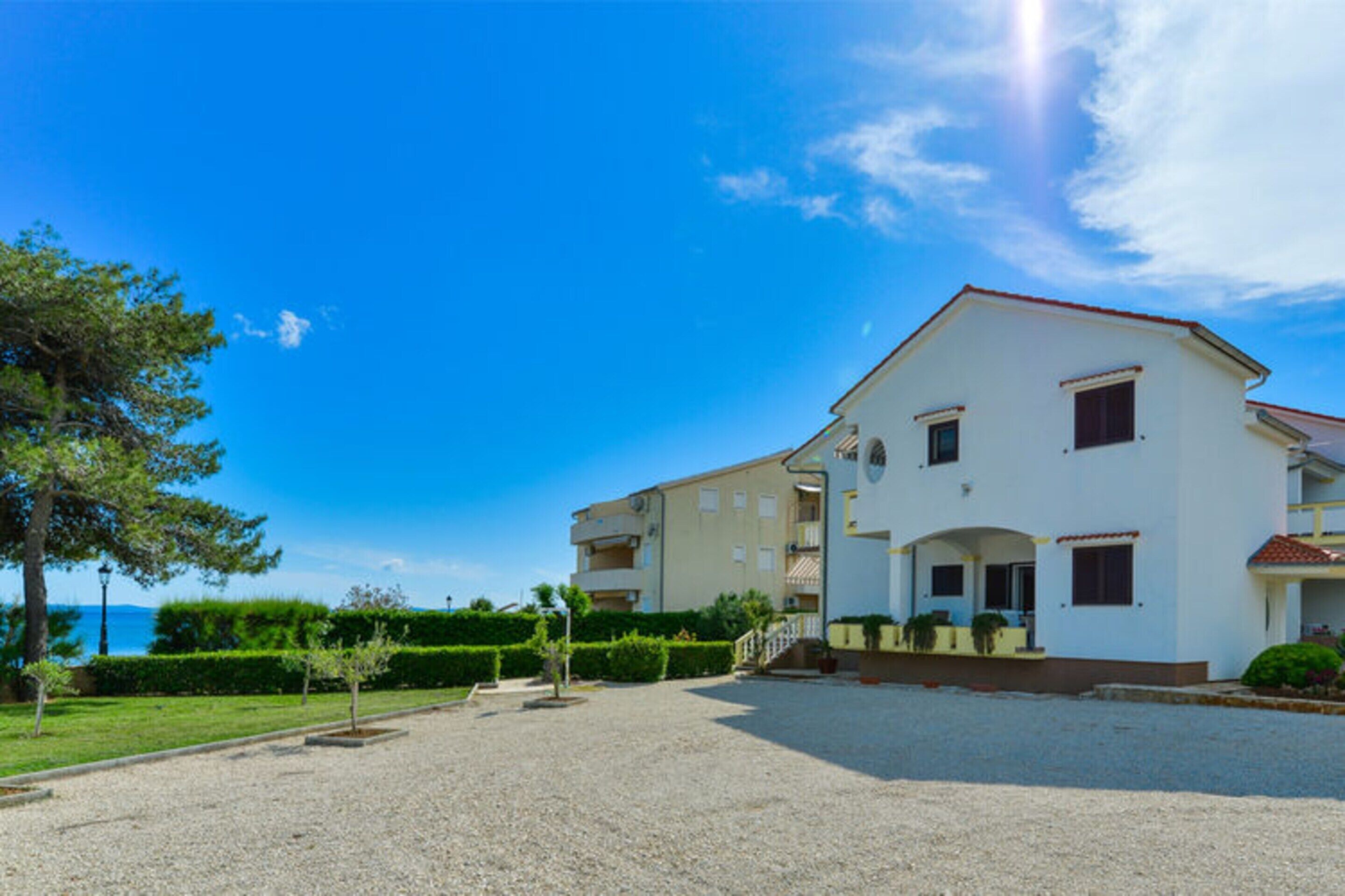 A two-story building with a white facade, multiple balconies, and a gravel driveway.