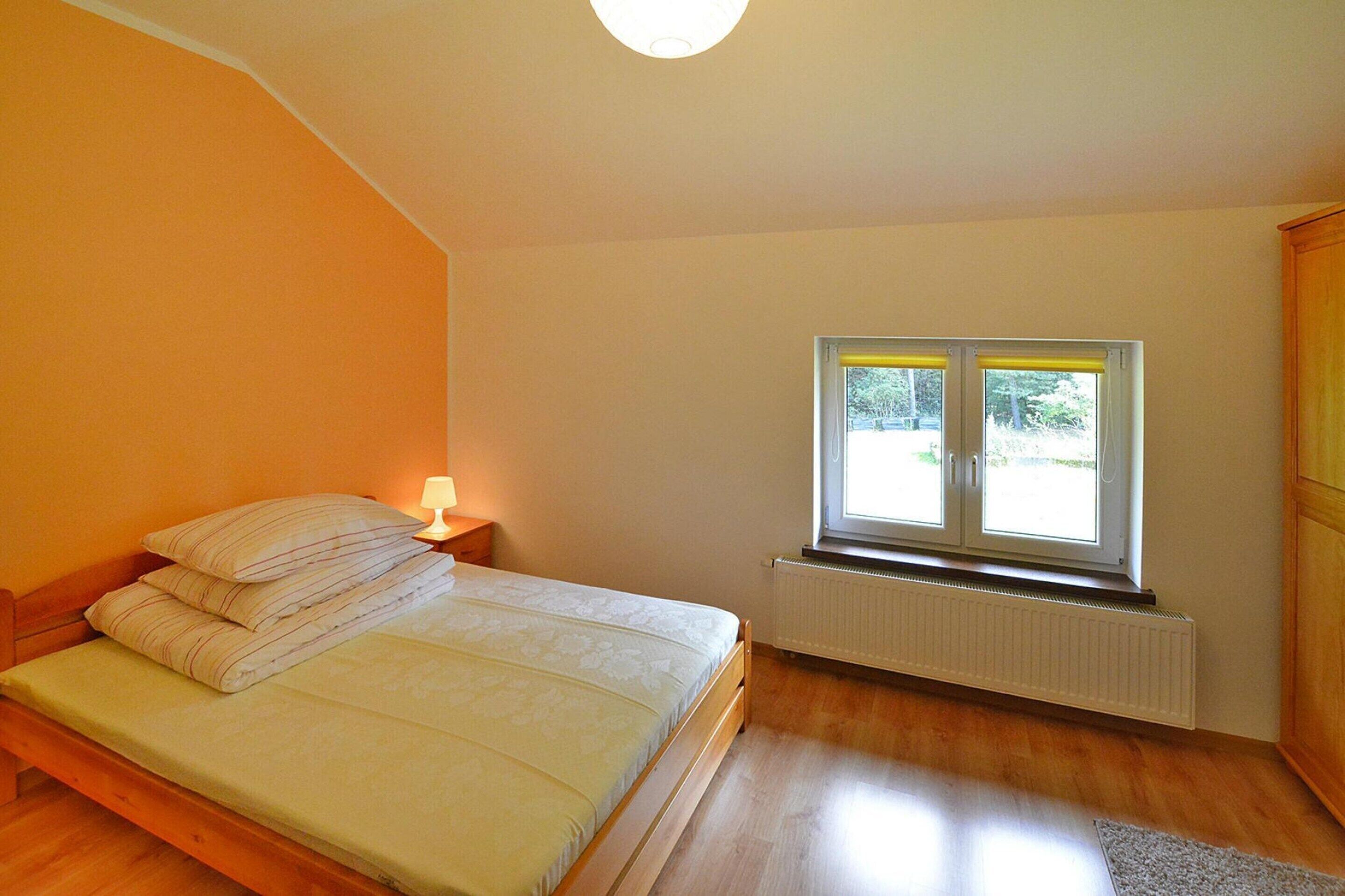 A bedroom with a bed, a window, a radiator, and a wooden wardrobe.