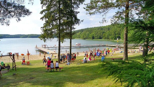 A lakeside park with picnic areas, a dock, and people enjoying the scenery. - Holiday Apartment in the Countryside, Biskupice (Biały Bór)