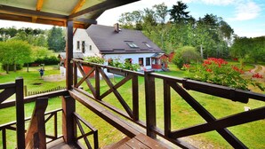 A wooden deck with a view of a house and garden. - Holiday Apartment in the Countryside, Biskupice (Biały Bór)