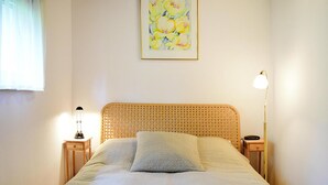 Ein ordentlich bezogenes Bett mit einer gemusterten Decke und Kissen, eine Nachttischlampe und ein gerahmtes Blumenbild an der Wand.