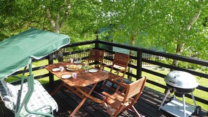 Eine Holzterrasse mit Tisch, Stühlen, einem Grill und einer überdachten Bank.