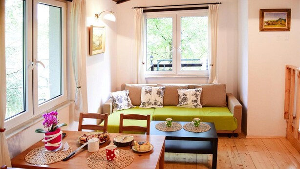 Ein gemütliches Zimmer mit Holzboden, einem grünen Sofa, einem Esstisch mit Stühlen und einem Fenster mit Vorhängen.