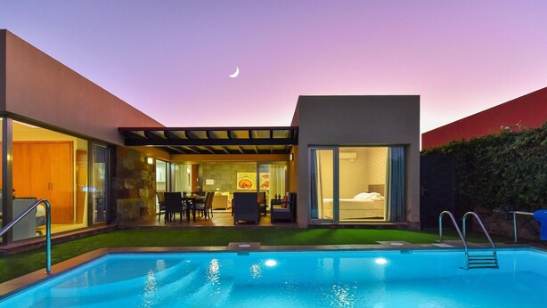 A modern house with a swimming pool, a patio with outdoor furniture, and a bedroom visible through a glass door. - Holiday Home, Maspalomas (San Bartolomé de Tirajana)