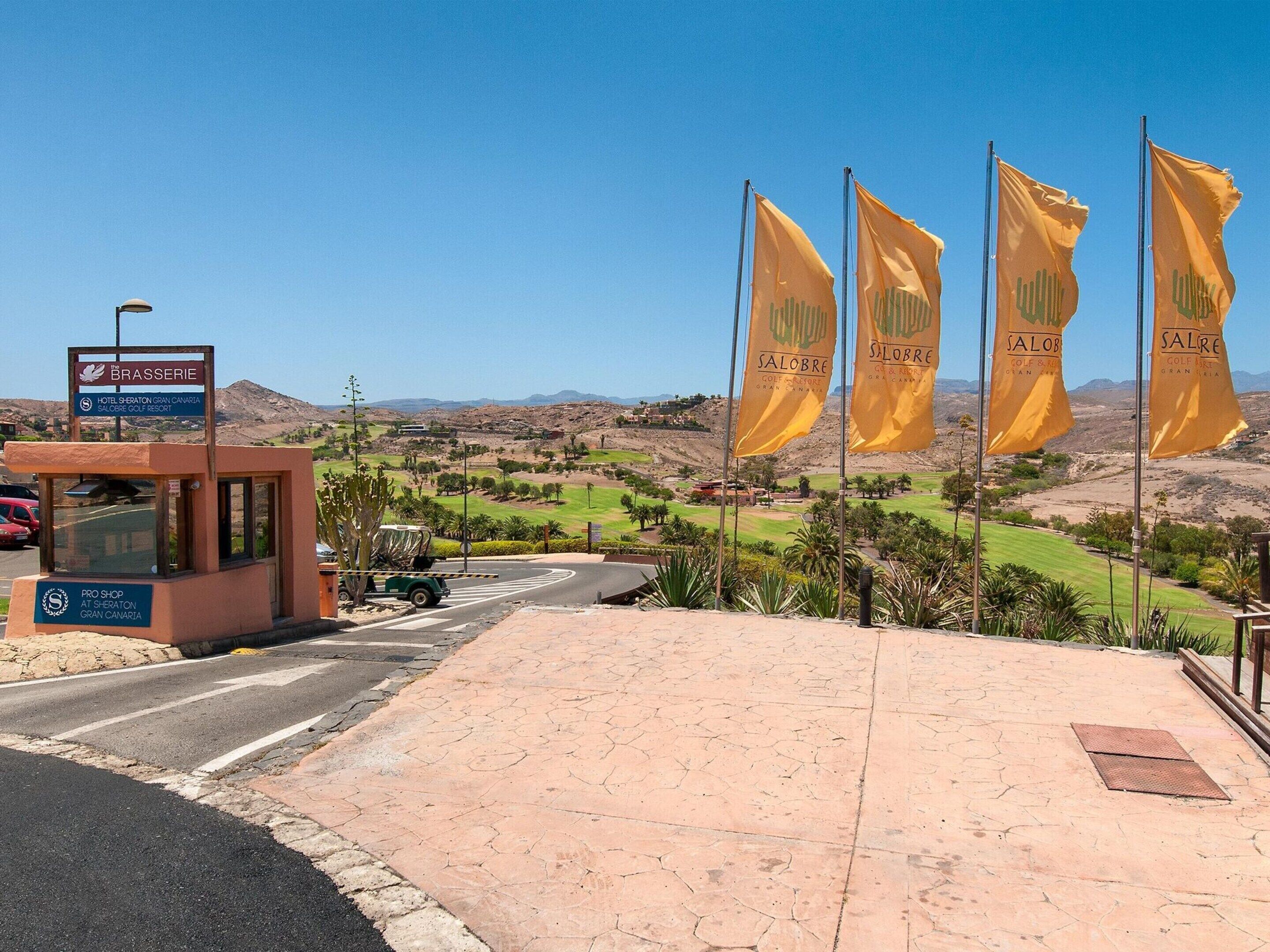 A hotel entrance with a sign for the Brasserie, a golf course in the background, and multiple yellow flags.
