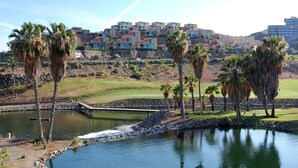 A golf course with a water feature, palm trees, and a large building with multiple balconies in the background. - Holiday Home, Maspalomas (San Bartolomé de Tirajana)