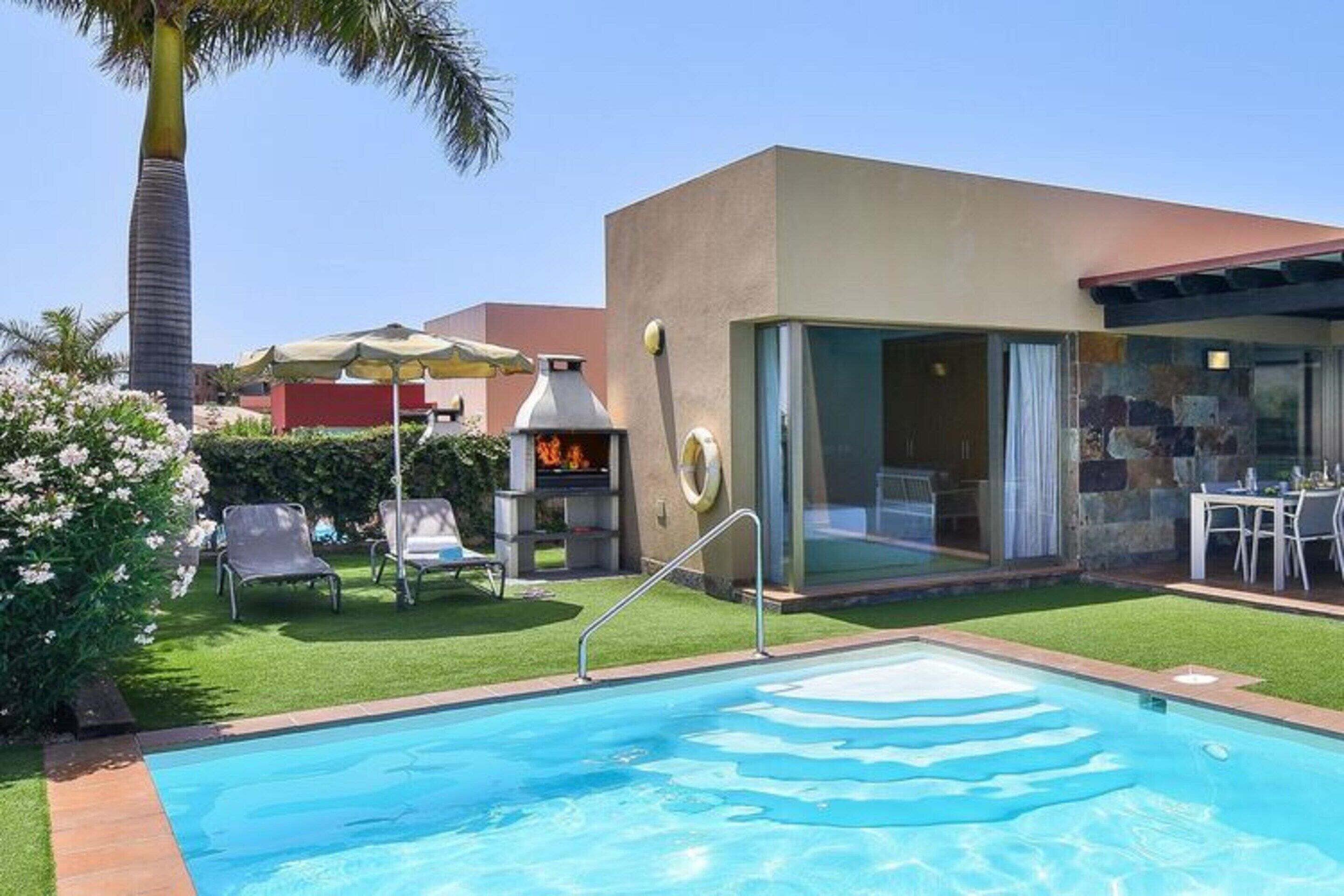 Una piscina con recinto in vetro, area salotto esterna e barbecue.