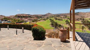 A stone-paved patio with a view of a golf course and distant hills. - Holiday Home, Maspalomas (San Bartolomé de Tirajana)
