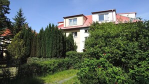 Un edificio de dos plantas con techo rojo, rodeado de abundante follaje y altos árboles.