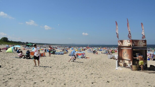 Escena de playa con un café, tiendas de campaña y gente relajándose.
