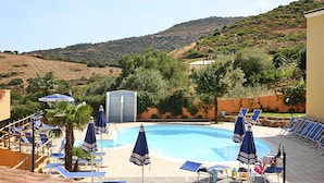 Un espace piscine doté de chaises longues et de parasols, entouré de collines et de verdure.