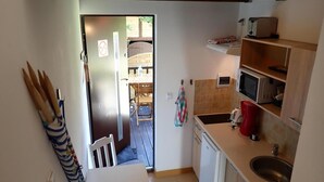 Kompakti keittiö, jossa on jääkaappi, mikroaaltouuni ja pesuallas. Ruokailutila näkyy avoimen oven läpi.