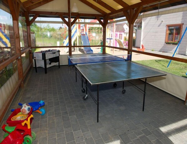 An outdoor covered area with a ping pong table, a foosball table, and a children's play area with toys. - Holiday Home in Sianozety Near the Beach (Ustronie Morskie)