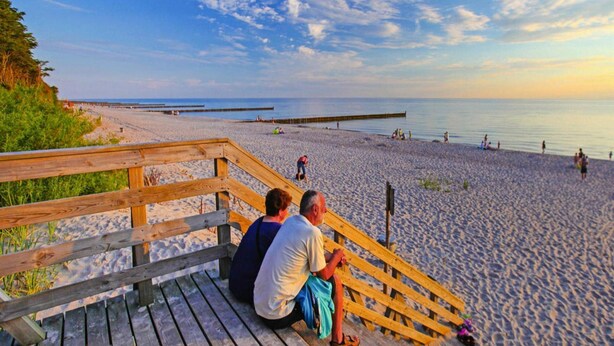 A wooden boardwalk leading to a sandy beach with a clear view of the ocean and a wooden pier extending into the water. - Holiday Home in Sianozety Near the Beach (Ustronie Morskie)
