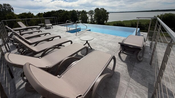 A rooftop pool area with lounge chairs, a small table, and a view of a lake.