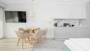 A modern hotel room with a dining area, kitchenette, and a bed.