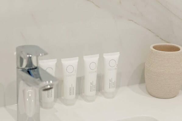 A bathroom with a modern faucet, three white toiletry tubes, and a textured ceramic container.