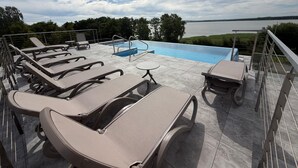 Un espace piscine aménagé sur le toit, avec des chaises longues, une petite table et une vue sur un lac.