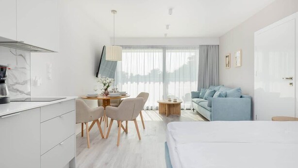 Une chambre d’hôtel moderne comprenant un lit, un coin repas avec des chaises et une table, un canapé et une grande fenêtre avec des rideaux.
