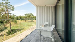 Un balcon avec deux chaises blanches, une porte vitrée et une vue sur un espace verdoyant avec des arbres.