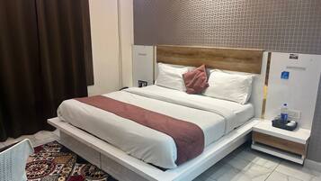 Habitación de hotel con una cama grande, una mesita de noche con una botella de agua y una alfombra estampada.