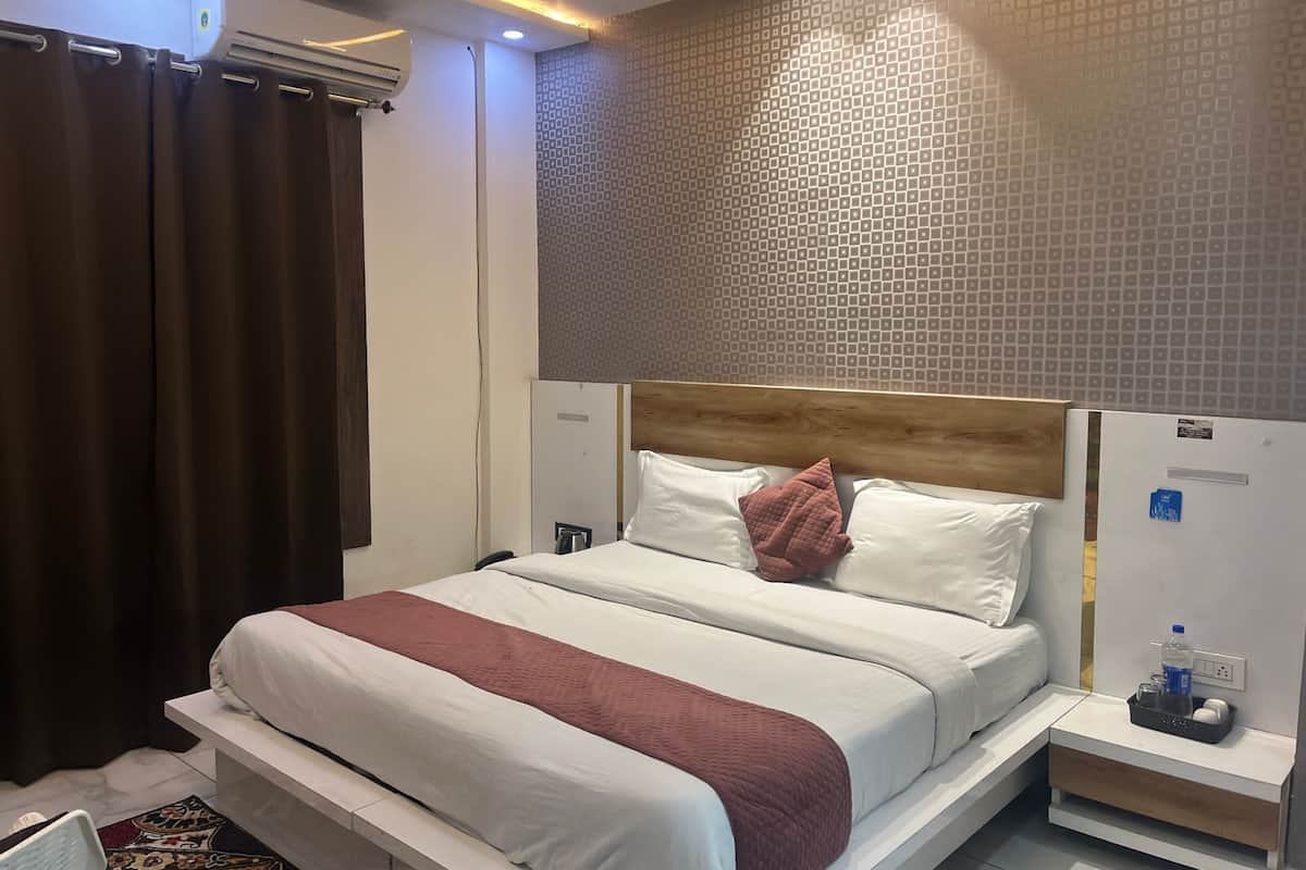 A hotel room with a bed, a nightstand, a wall-mounted air conditioner, and a patterned wall.