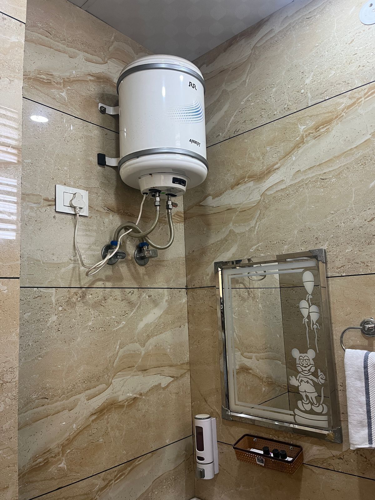 A bathroom with a wall-mounted water heater, a hand dryer, and a Mickey Mouse-themed mirror.