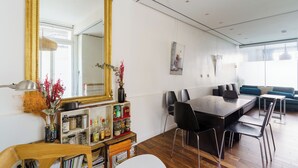 A modern dining area with a large mirror, wooden shelves with kitchen items, and a dining table with chairs.
