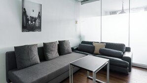 A modern living room with a grey sofa, a small table, and a large window with a view of a building.