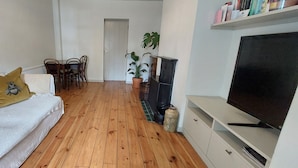 Ein Wohnzimmer mit einer Couch, einem Fernseher, einem Esstisch mit Stühlen und einer Zimmerpflanze.