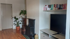 Ein Wohnzimmer mit einem Flachbildfernseher, einem Bücherregal voller Bücher, einer Topfpflanze und Holzdielen.