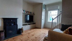 Ein Wohnzimmer mit Kamin, Fernseher, Bücherregal und einer Treppe, die zu einer oberen Etage führt.